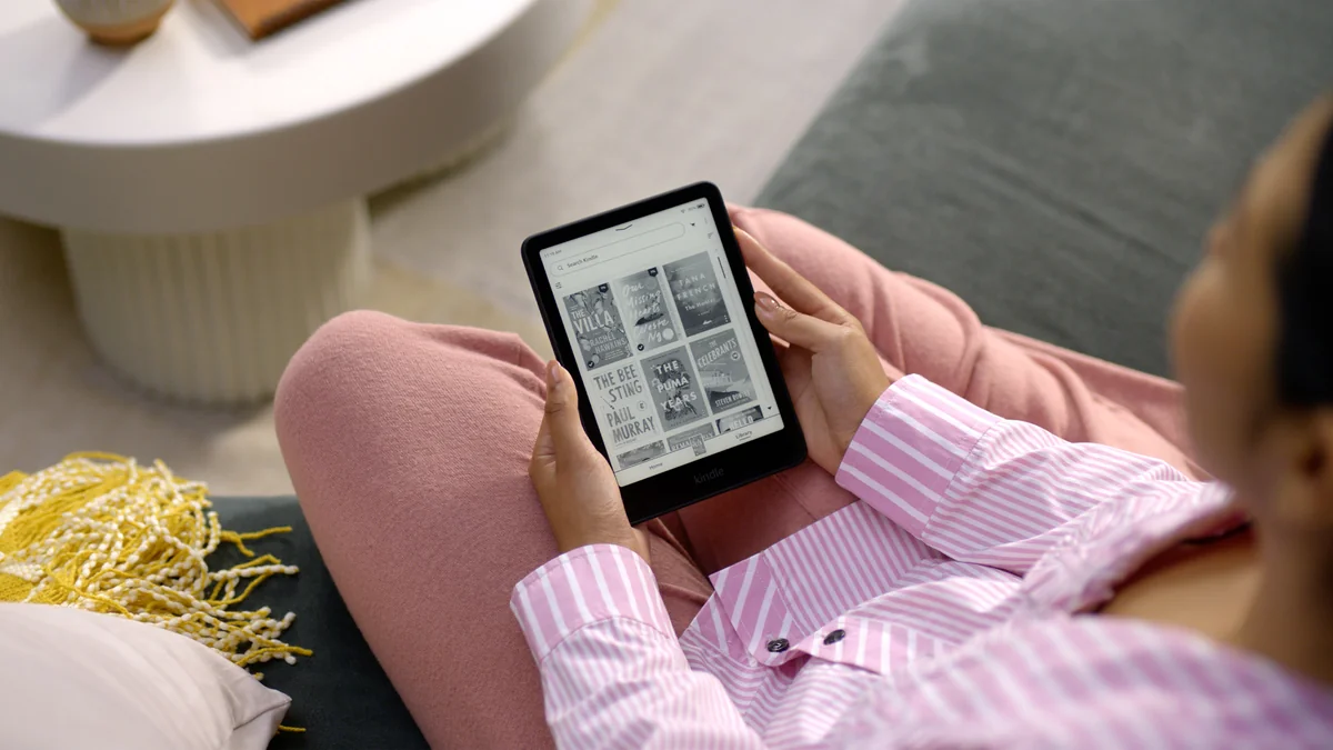 A reader holding a Kindle Paperwhite on a sofa